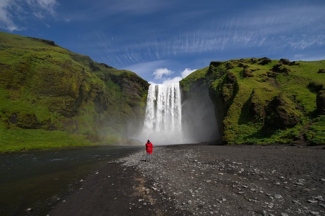 A single high waterfall dropping into a green plain in southern Iceland